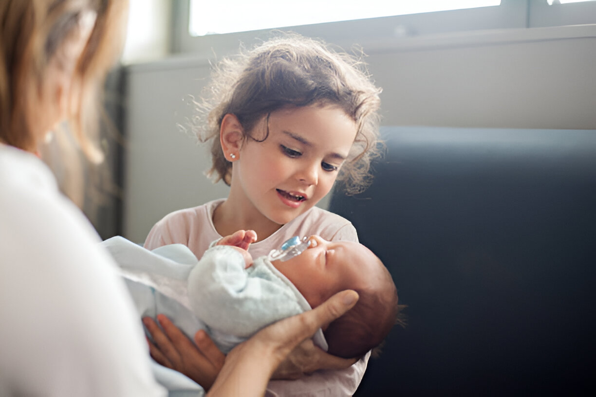 Young girl lovingly gazes at her newborn sibling, symbolizing the beauty of baby birth and family bonding.