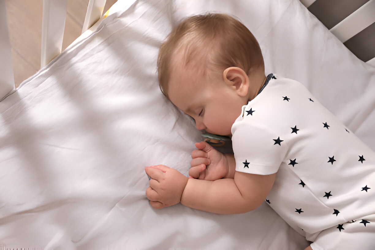 Baby peacefully sleeping in crib during contact nap, dressed in a white onesie with black stars, promoting safe and comforting sleep.