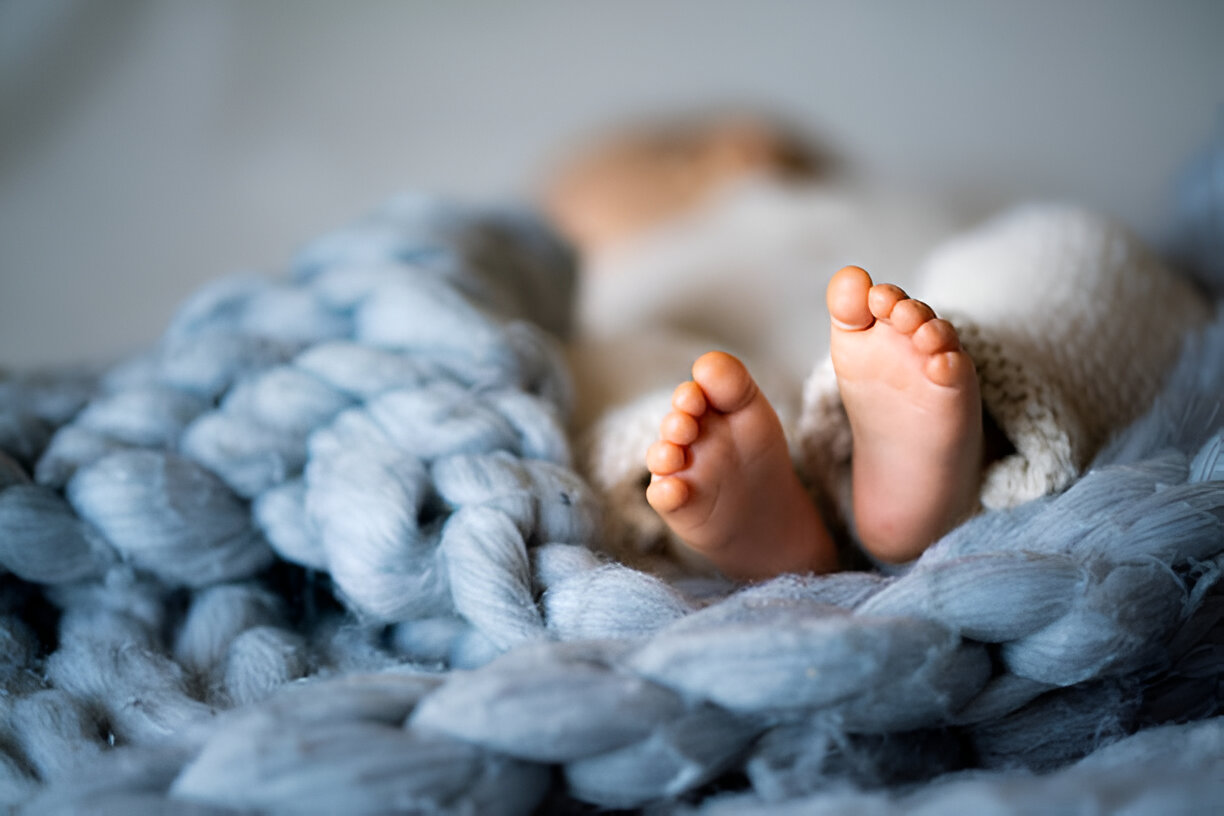 Close-up of a newborn's tiny feet wrapped in a soft blue knitted blanket, emphasizing the warmth and tenderness of newborn care.